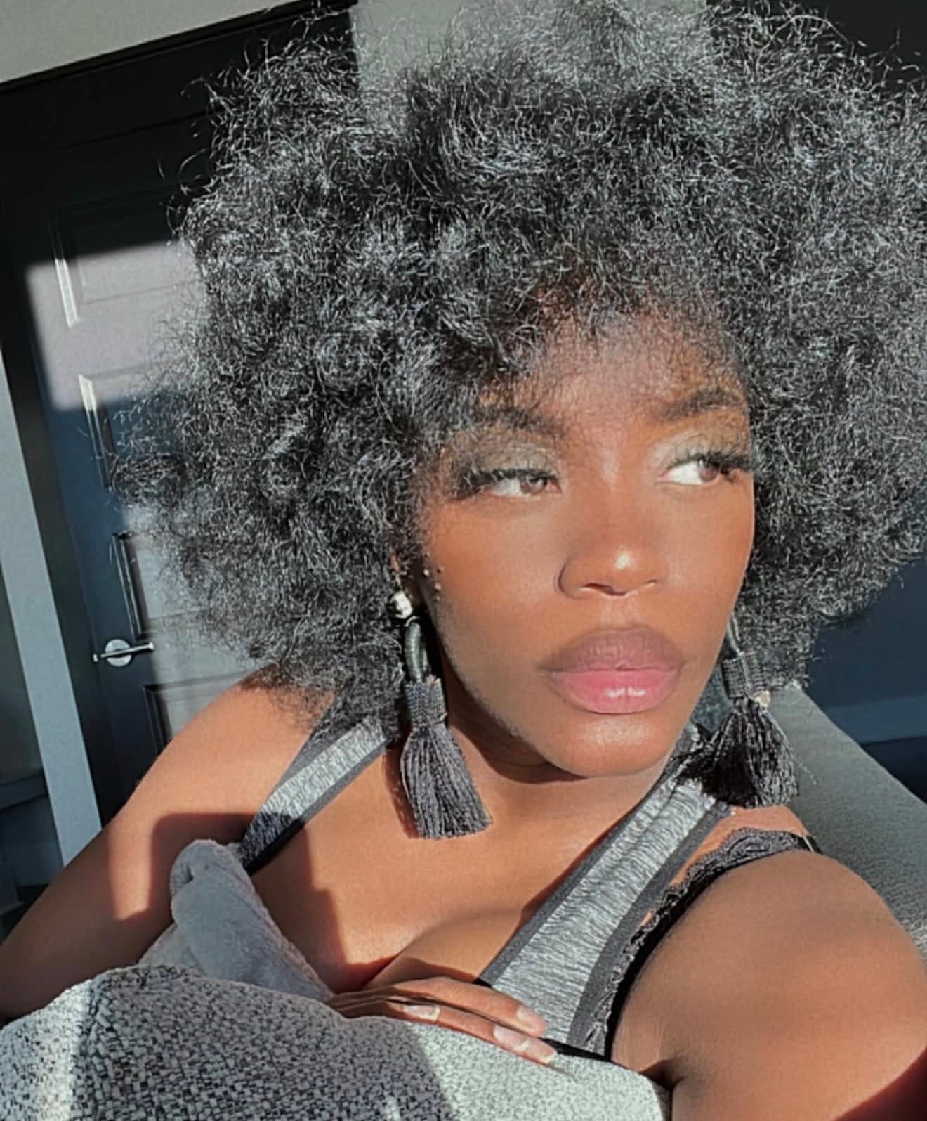 Tiyane Clarke in sunlight with natural hair and black tassel earrings, looking off-camera.
